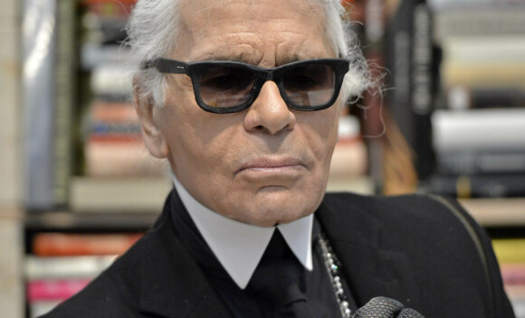 FILE - In this Friday, Feb. 14, 2014 file photo, Karl Lagerfeld poses for photographers in front of his books prior to the start of an exhibition at the museum Folkwang in Essen, Germany. Chanel's iconic couturier, Karl Lagerfeld, whose accomplished designs as well as trademark white ponytail, high starched collars and dark enigmatic glasses dominated high fashion for the last 50 years, has died. He was around 85 years old. (AP Photo/Martin Meissner, File )